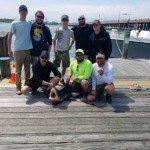 Eight anglers on a dock posing with a large fish