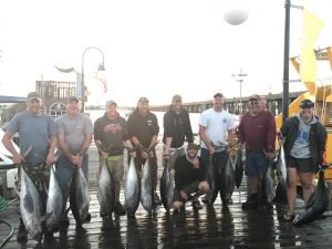Nine anglers each holding large fish on wet dock