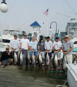 Seven anglers each holding large fish with crew member kneeling beside
