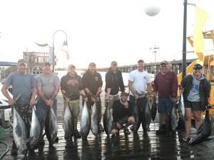 Nine anglers holding a handful of large fish on wet dock